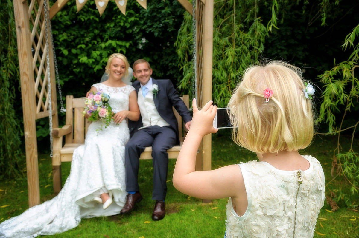 Flower girl taking photo of bride and groom